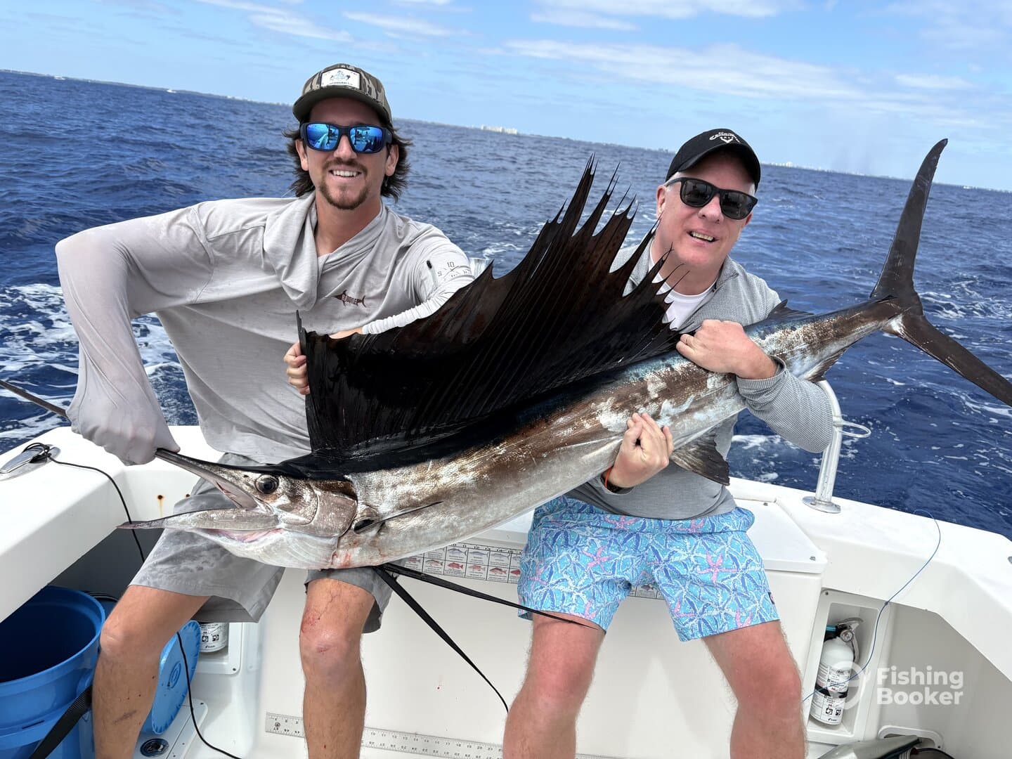 Two anglers proudly displaying a large Sailfish aboard a fishing boat in open waters.