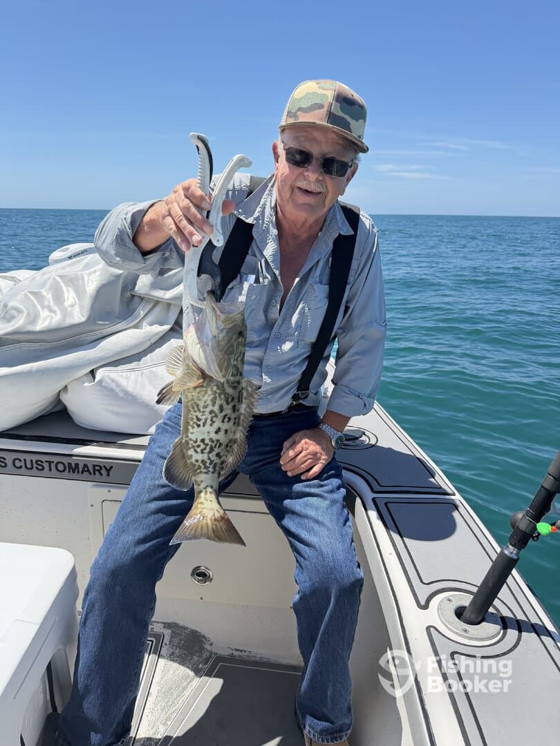 An angler proudly displaying a large Grouper caught while fishing on a boat in clear waters.