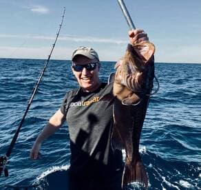 Angler proudly displaying a large Grouper while fishing offshore, showcasing a vibrant blue ocean backdrop.