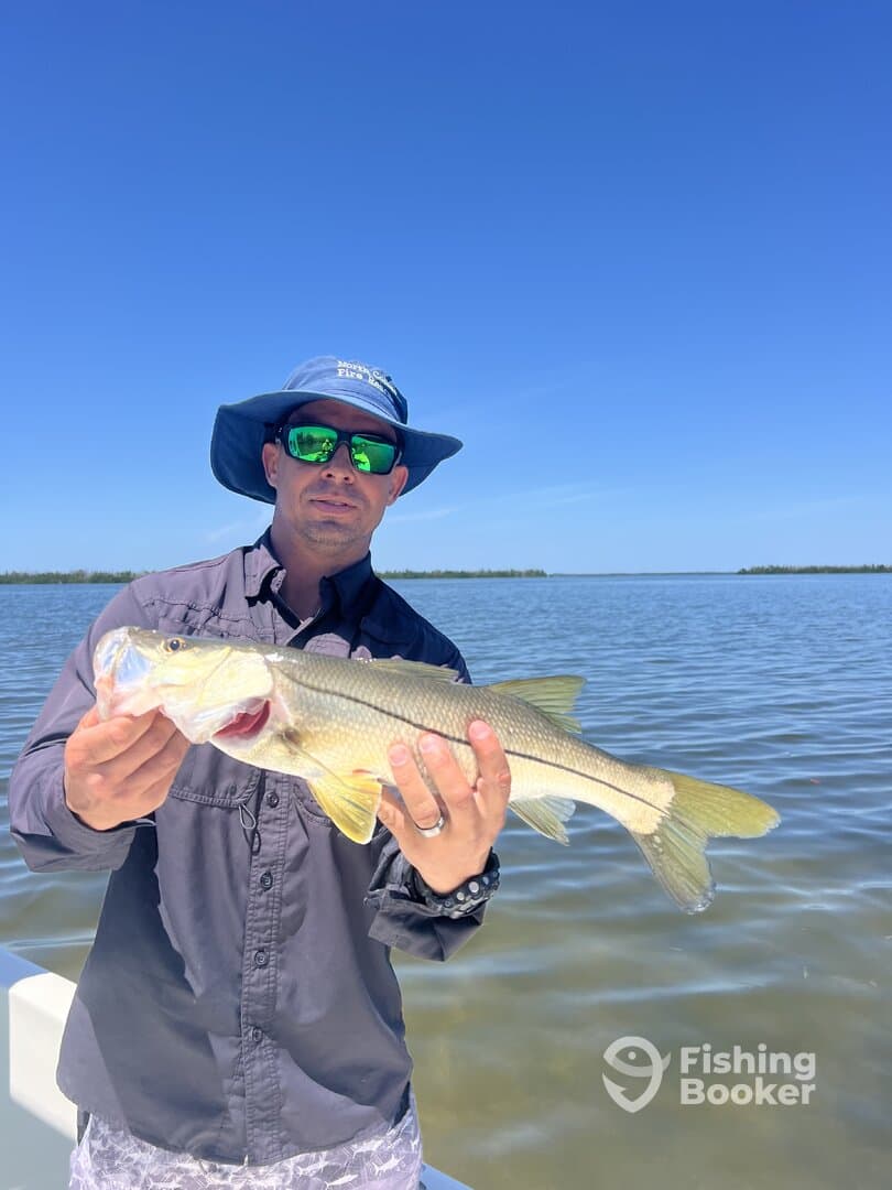 Angler proudly displaying a Snook while fishing in a scenic coastal environment.