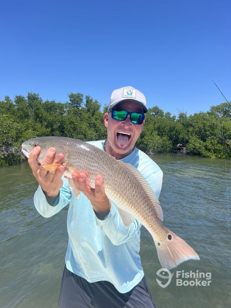 A proud angler displaying a large Redfish while enjoying a sunny day on the water.