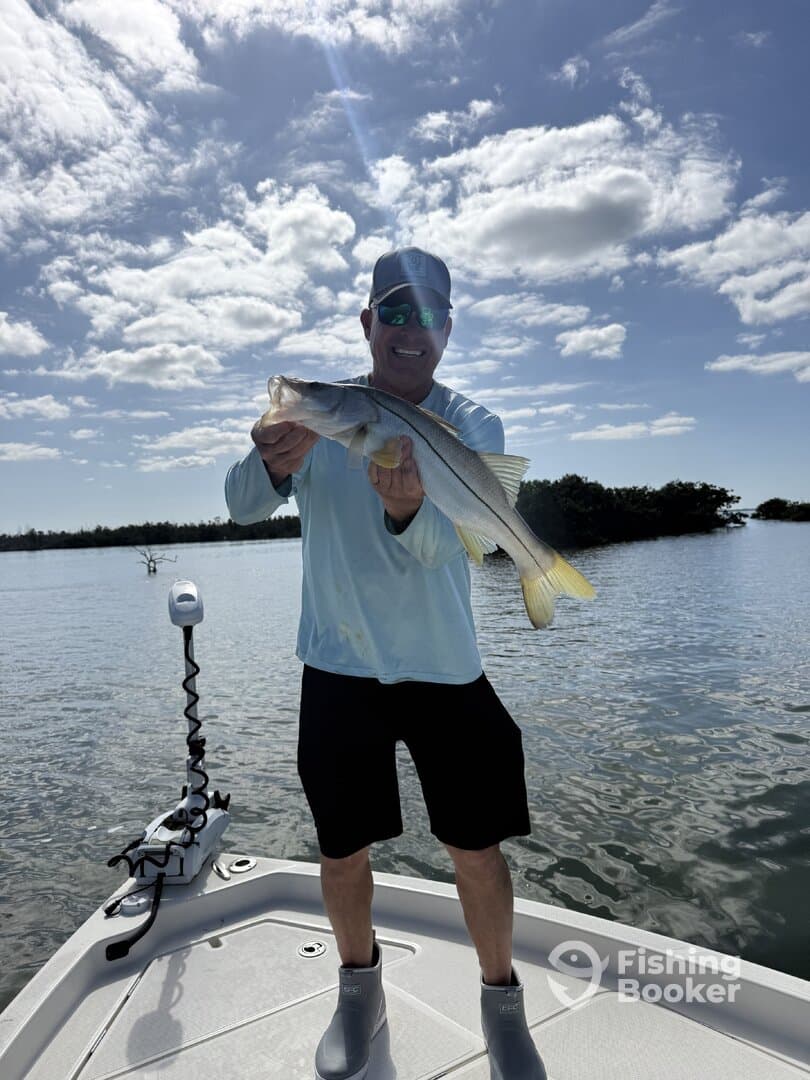 Angler proudly displaying a large Snook while fishing on a sunny day in a coastal waterway.