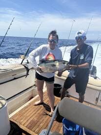 Two anglers proudly displaying a large fish on a charter boat, enjoying a sunny day on the open water.