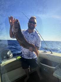Angler proudly displaying a large Grouper while fishing on a boat in open waters.