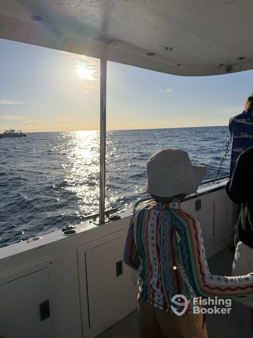 A young child enjoying a scenic view from inside the boat, with the sun setting over the ocean.