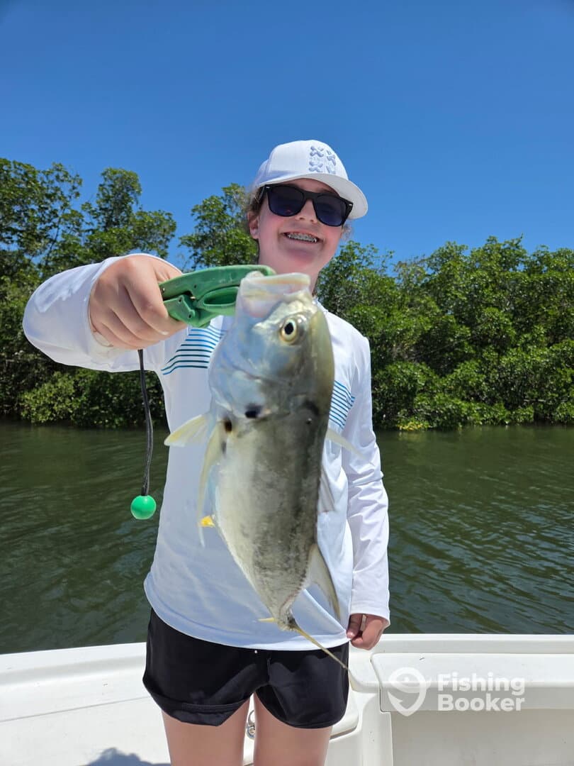 A young angler proudly displaying a fish while fishing in a scenic waterway, showcasing a bright sunny day.