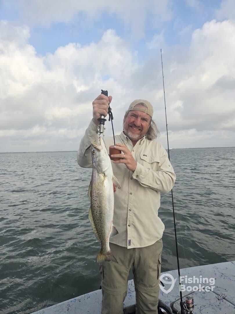 Angler proudly displaying a large Speckled Trout while fishing on a boat in open waters.