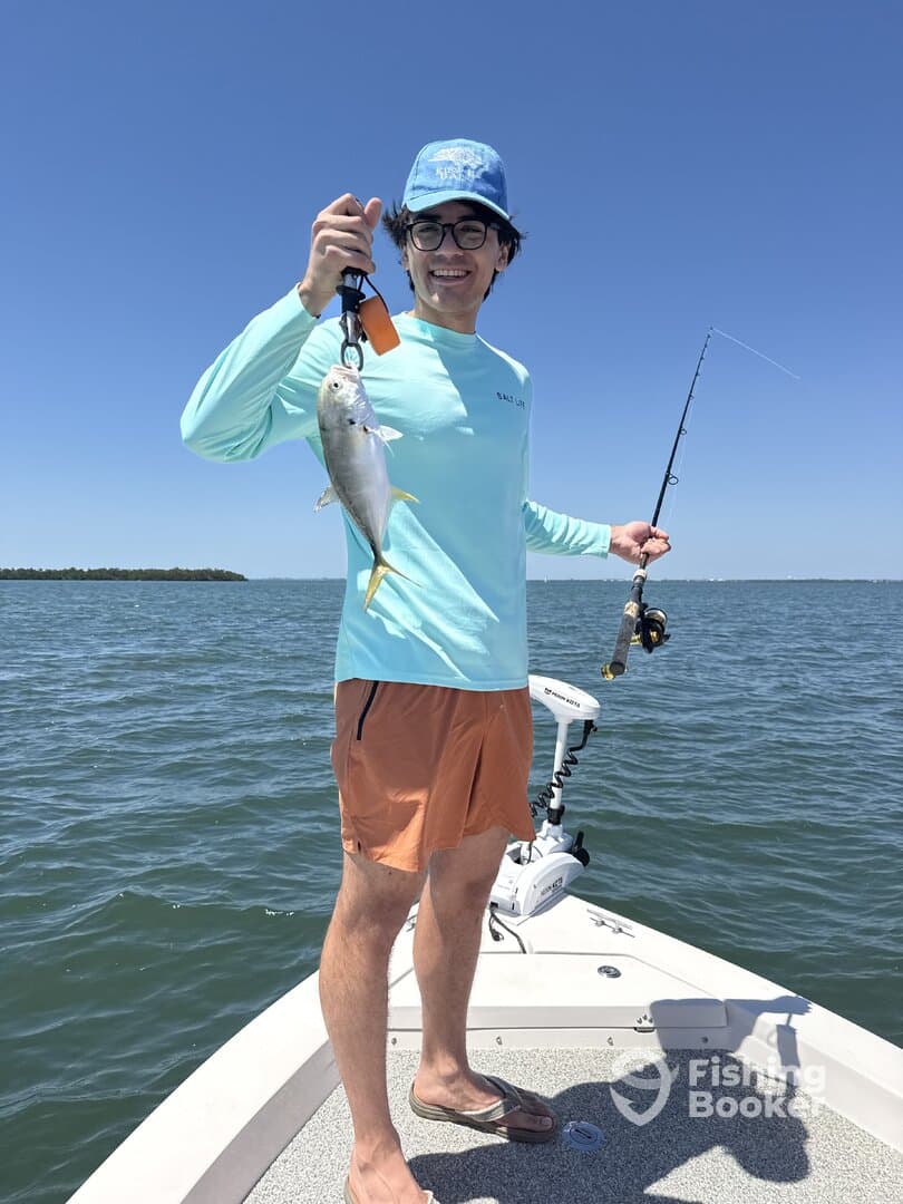 A young angler proudly displaying a small fish while fishing on a sunny day, showcasing the excitement of a successful catch.