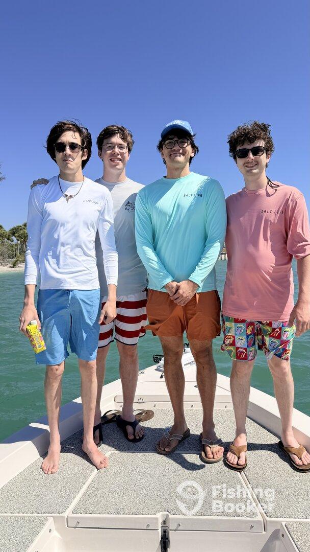 A group of four young adults posing on the bow of a boat, enjoying a sunny day on the water.