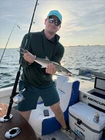 Angler proudly displaying a Spanish Mackerel while fishing on a boat in a sunny coastal environment.