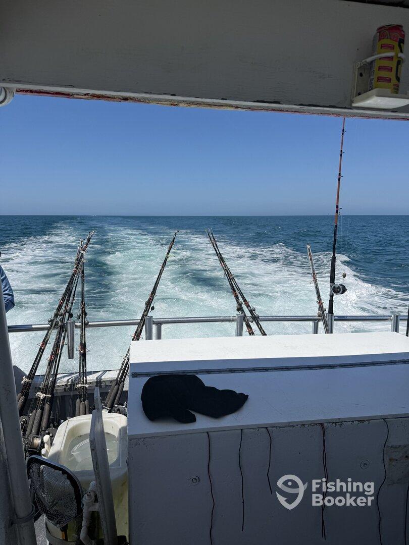 View from the helm of a fishing boat, showcasing multiple fishing rods and the wake left behind as it moves through the ocean.