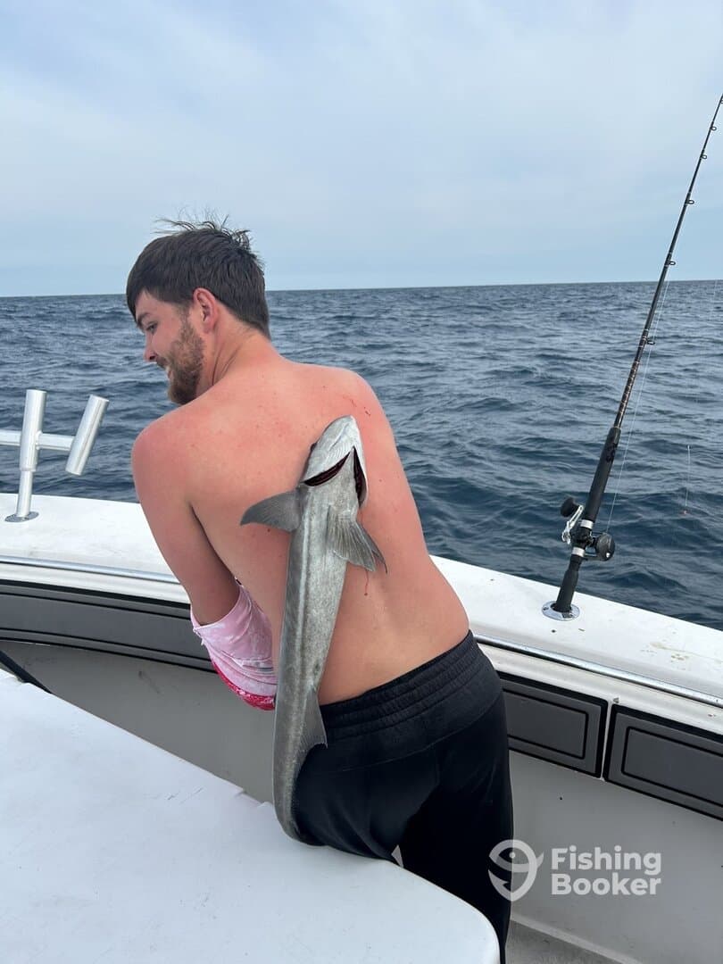 Angler playfully posing with a fish on his back while fishing on a boat in open waters.
