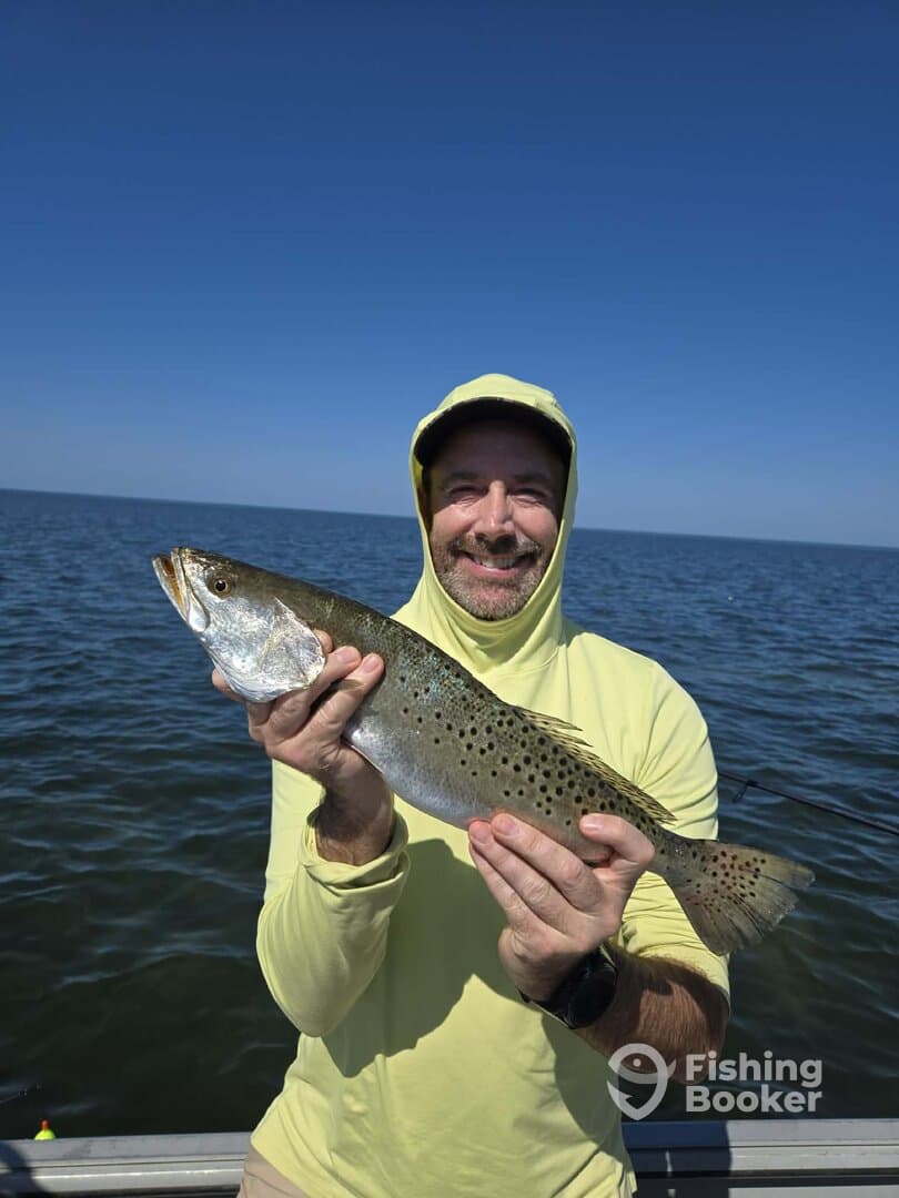 Angler proudly displaying a large Speckled Trout while fishing on a boat in open waters.