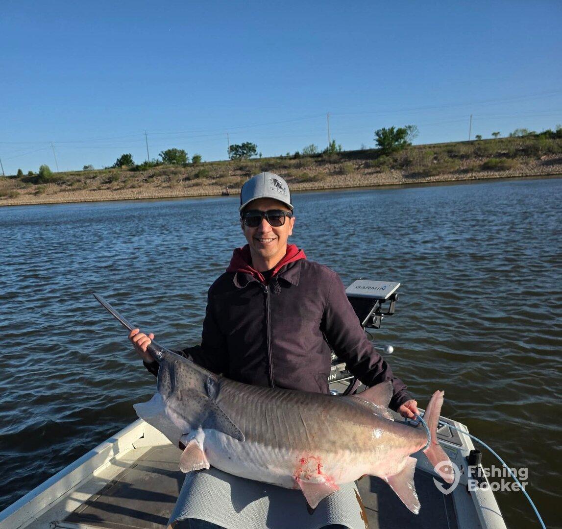 Angler proudly displaying a large Catfish while fishing on a calm lake.