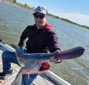 Angler proudly displaying a large fish while seated in a boat on a sunny day, showcasing a successful catch.