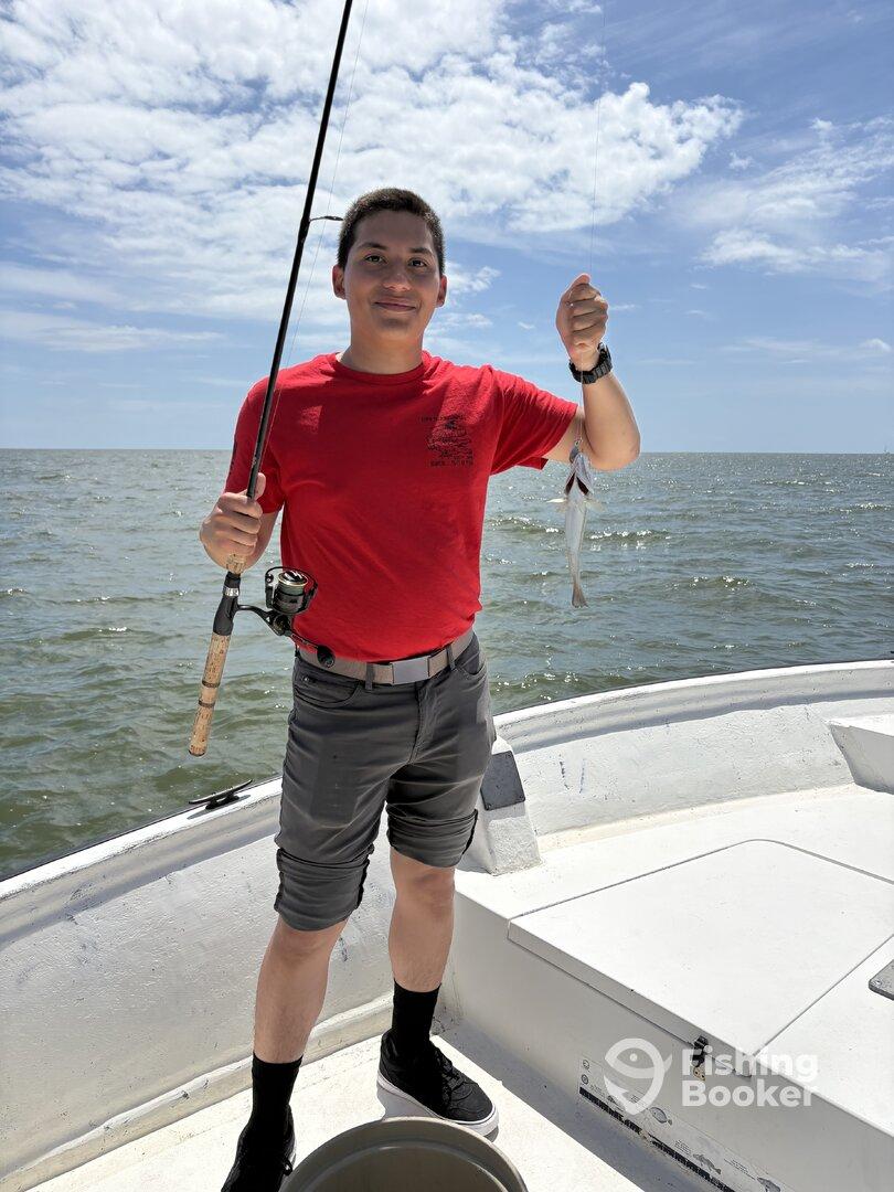 A young angler proudly displaying a caught fish while fishing on a boat in open waters.
