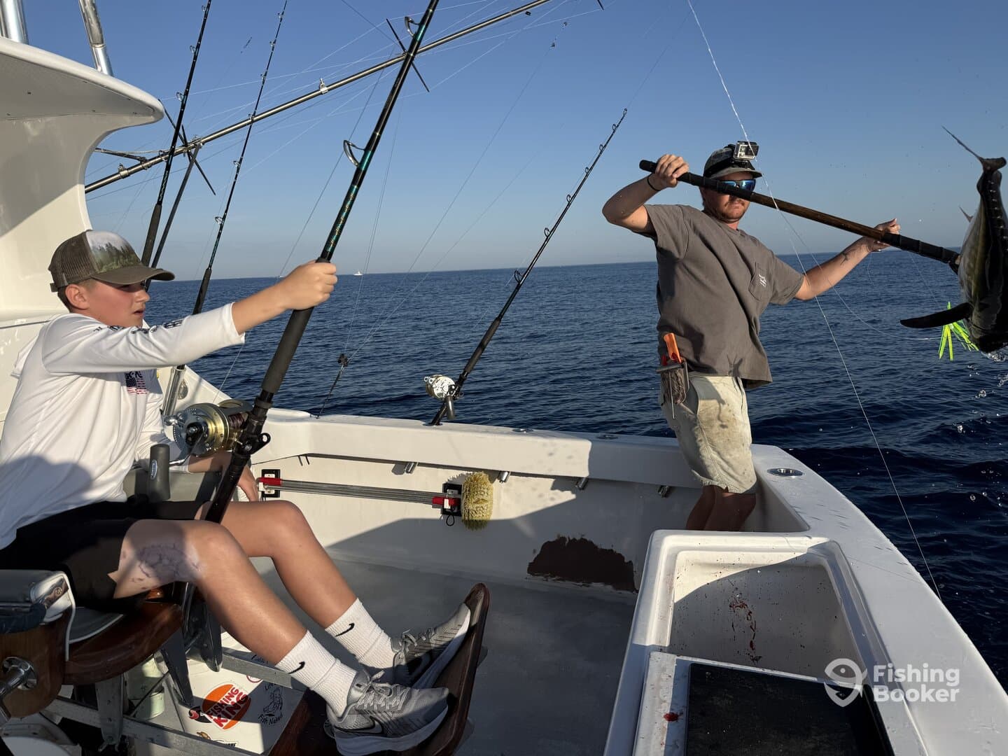 A young angler is actively reeling in a fish while an adult prepares to land a large catch on a deep-sea fishing trip.