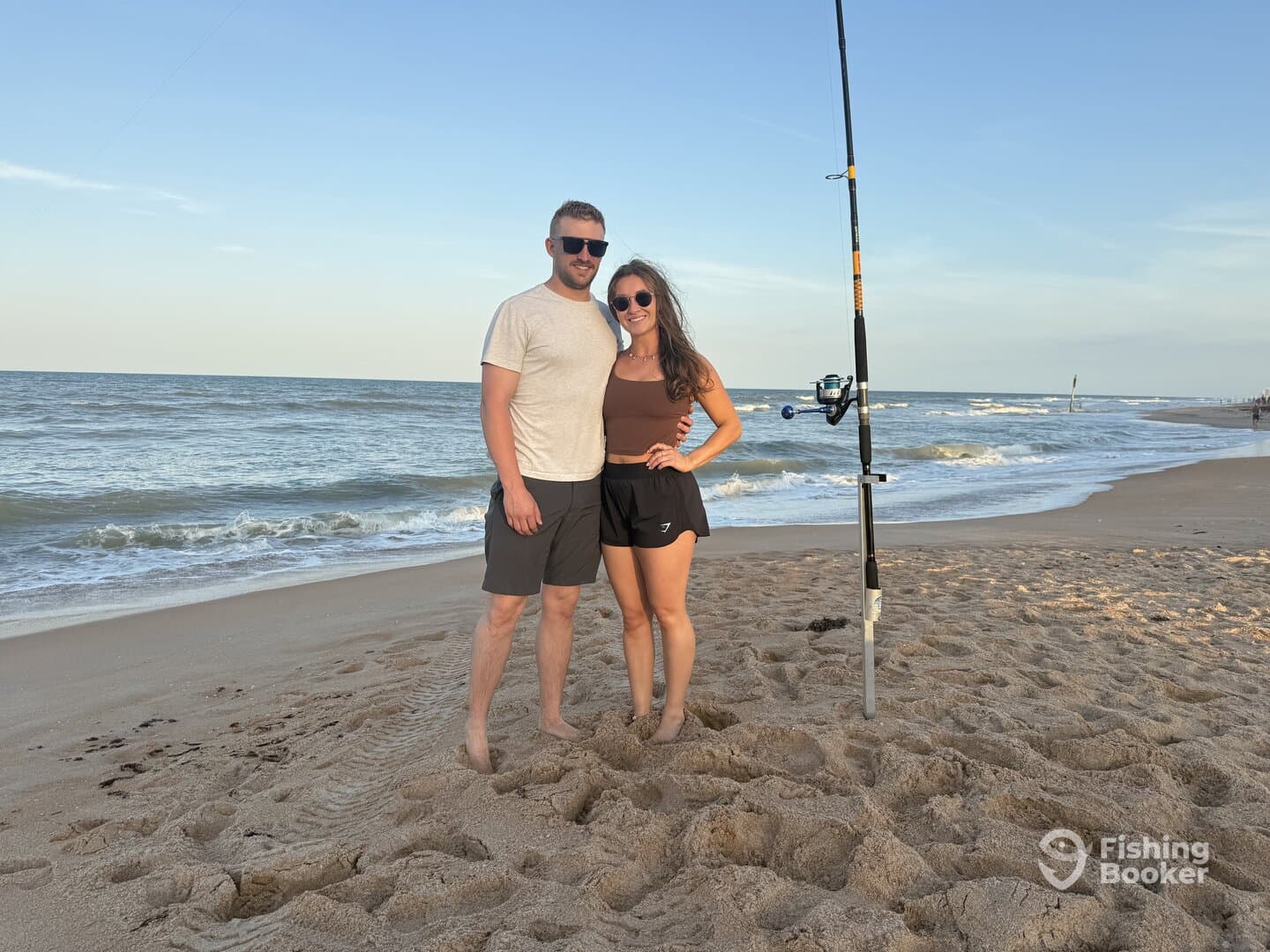 A couple poses on the beach with a fishing rod, enjoying a day by the ocean.