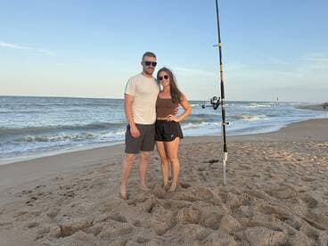 A couple poses on the beach with a fishing rod, enjoying a day by the ocean.