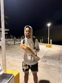 Angler proudly displaying a large Redfish at the dock during a nighttime fishing trip.