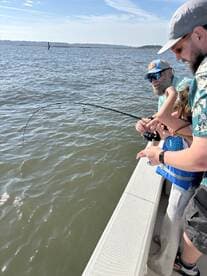 A family is engaged in fishing, with a child actively reeling in a catch while enjoying a sunny day on the water.