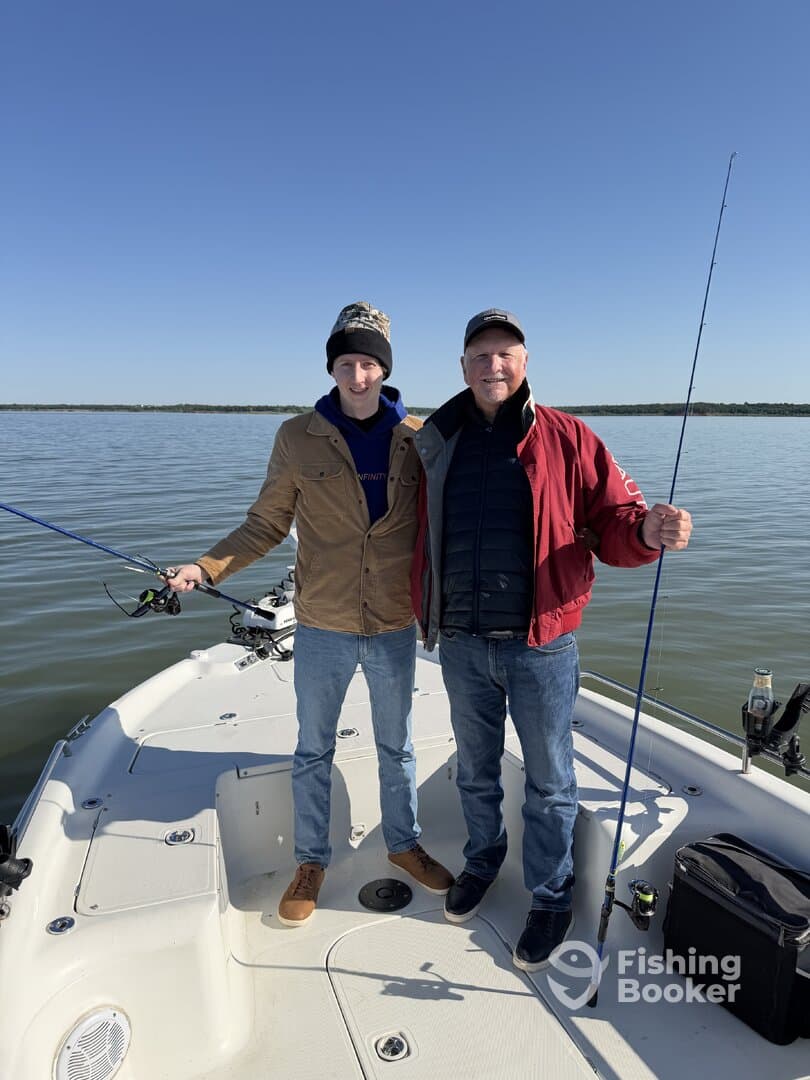 A father and son enjoying a fishing trip together on a boat, both holding fishing rods with a calm water backdrop.