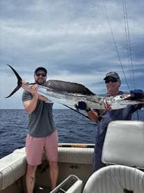 Two anglers proudly displaying a large Sailfish aboard a boat, showcasing their successful catch during a deep-sea fishing trip.