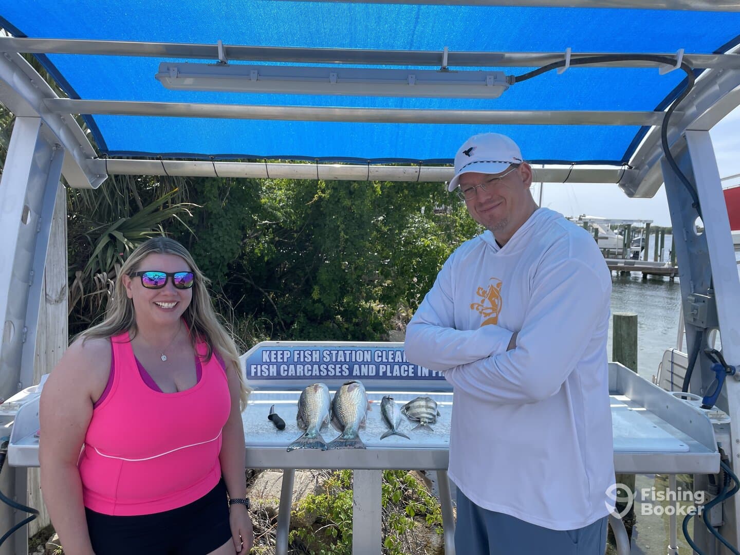 Two anglers proudly displaying their catch of fish at a cleaning station near the dock, enjoying a sunny day on the water.