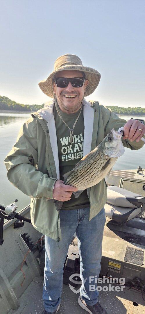 Angler proudly displaying a striped bass while fishing on a calm lake, showcasing a relaxed outdoor experience.