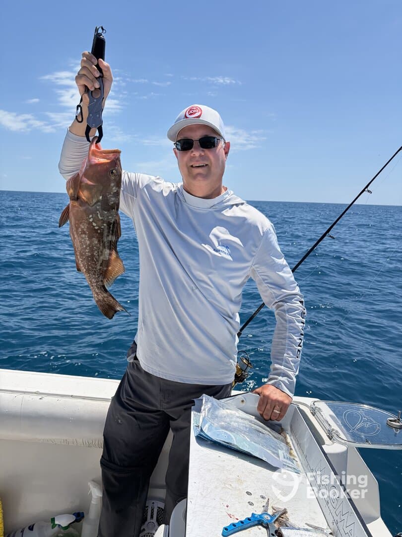 Angler proudly displaying a large Grouper while fishing on a sunny day in open waters.