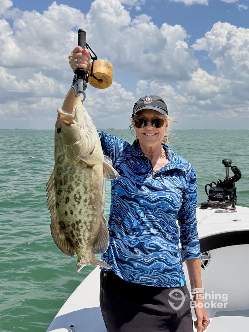 A proud angler holding a large Goliath Grouper while fishing on a sunny day in coastal waters.