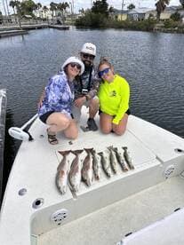A group of three anglers proudly displaying their catch of Redfish and Speckled Trout on the boat after a successful fishing trip.