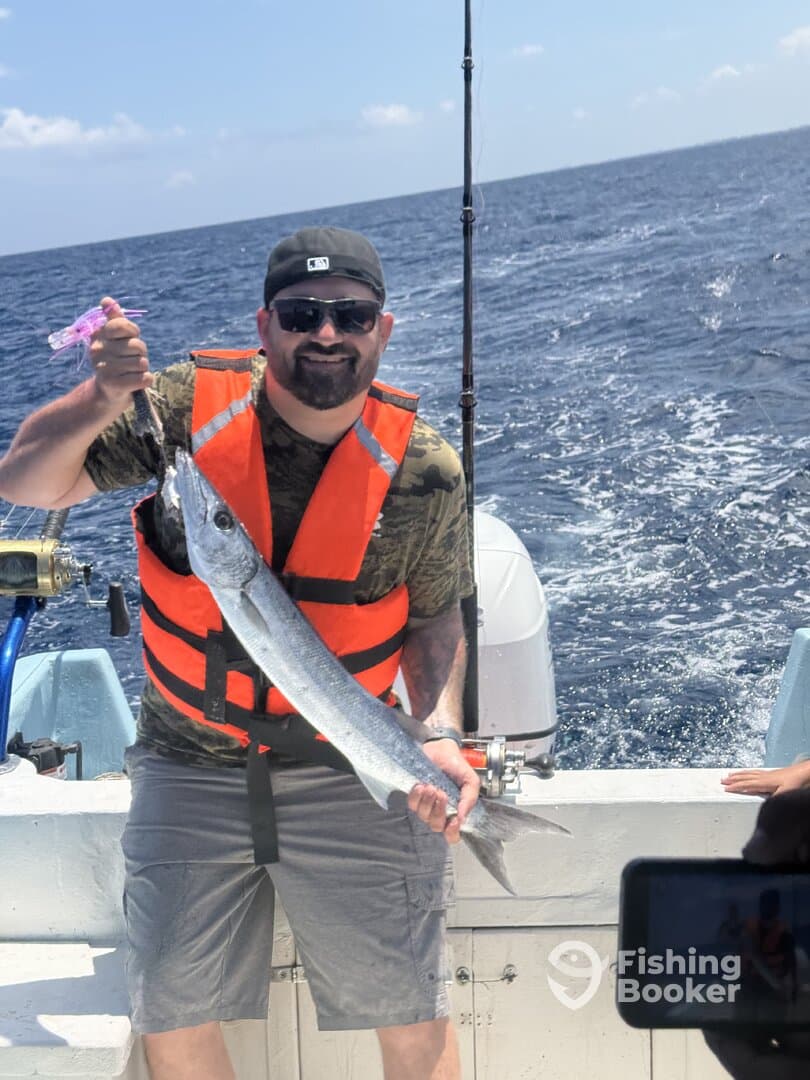 Angler proudly displaying a large Barracuda while fishing offshore, showcasing a vibrant blue ocean backdrop.
