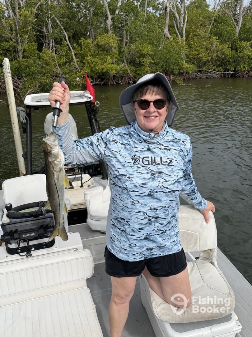 A proud angler holding a large Snook while fishing from a boat in a mangrove-lined waterway.