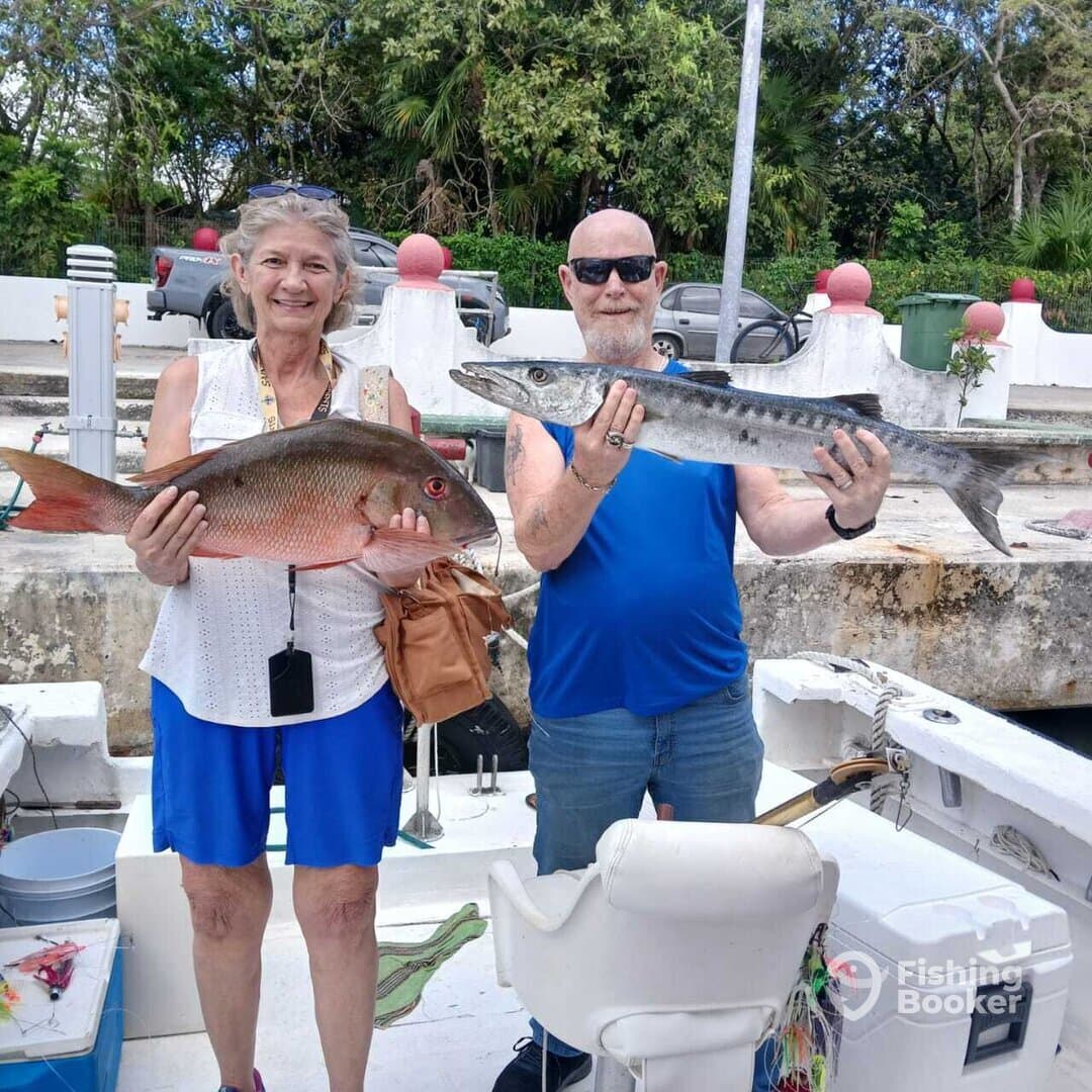 Two anglers proudly displaying their catches, a Snapper and a Barracuda, on a fishing trip.