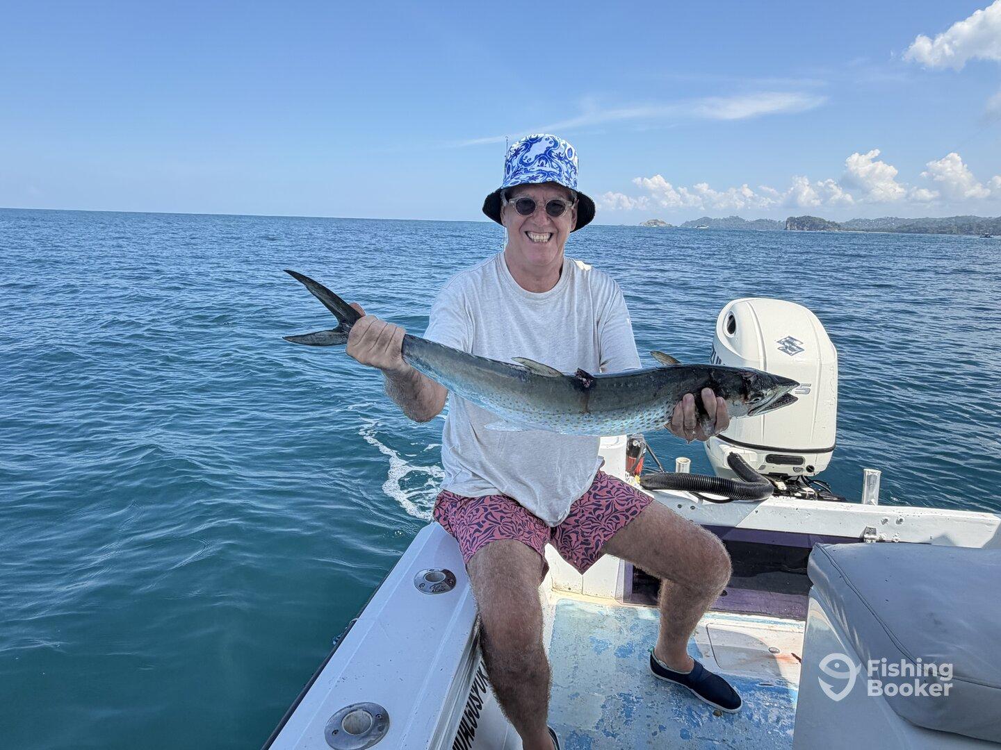 An angler proudly displaying a large fish while seated on a boat in clear blue waters, showcasing a successful fishing trip.