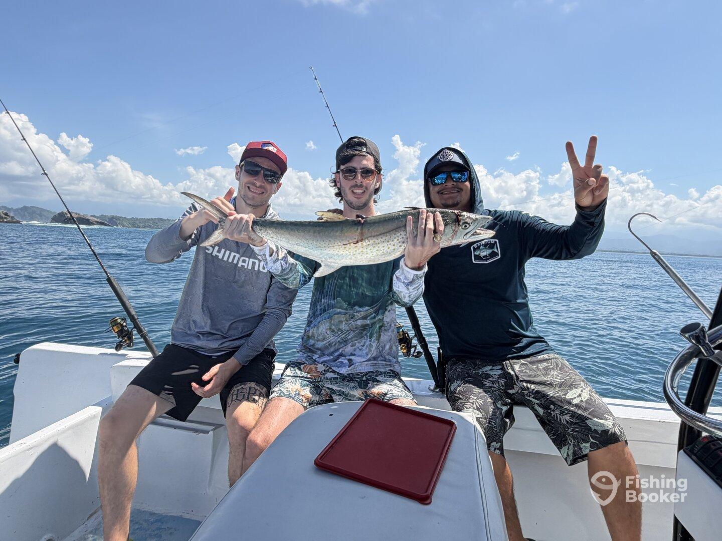 Three anglers proudly displaying a large fish while enjoying a sunny day on the water.