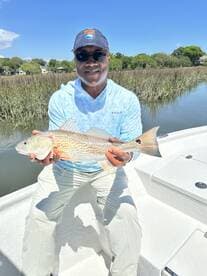 Angler proudly displaying a Redfish while fishing in a scenic marsh environment.