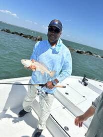 Angler proudly displaying a Redfish while fishing from a boat in a coastal environment.
