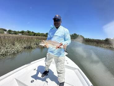 Angler proudly displaying a Redfish while fishing in a scenic marsh environment.