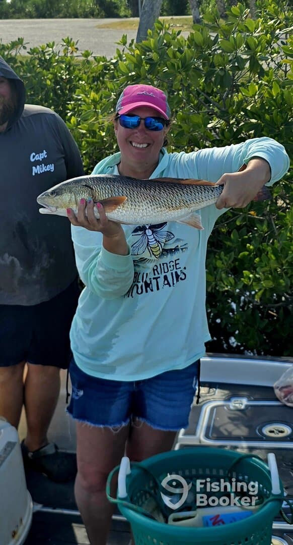 A proud angler displaying a large Redfish caught during a fishing trip, with a scenic backdrop of mangroves.