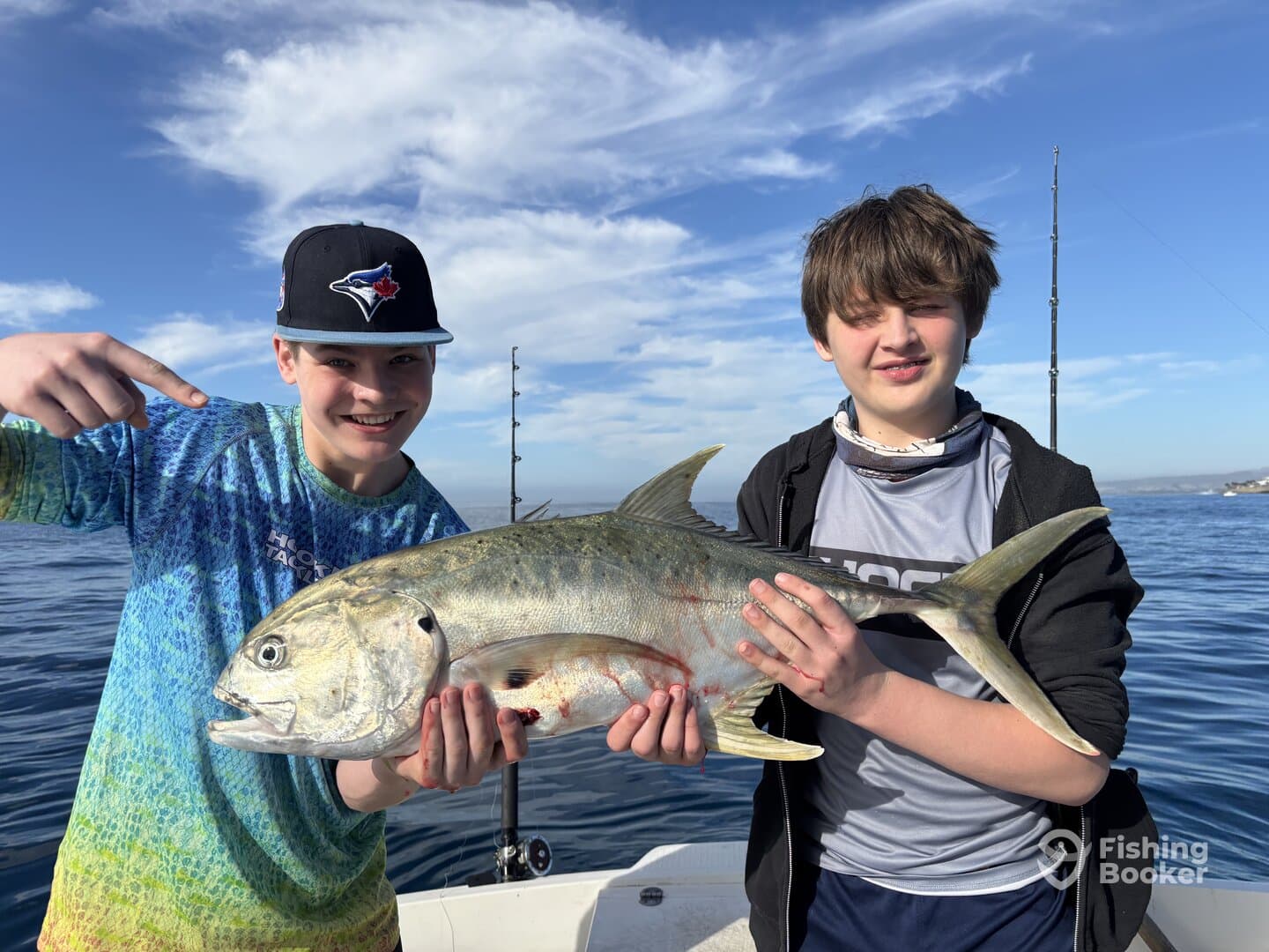 Two young anglers proudly displaying their catch, a large fish, while fishing on a boat in clear blue waters.