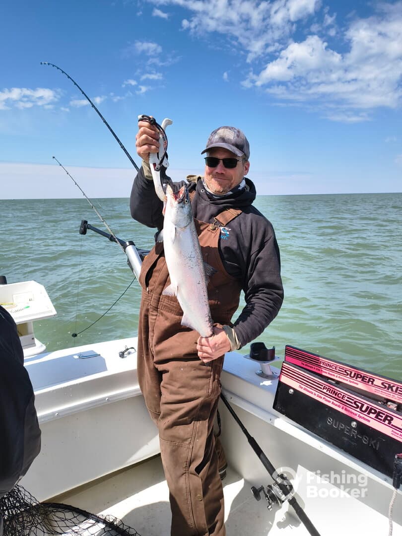 Angler proudly displaying a large trout while fishing on a boat, showcasing a successful day on the water.