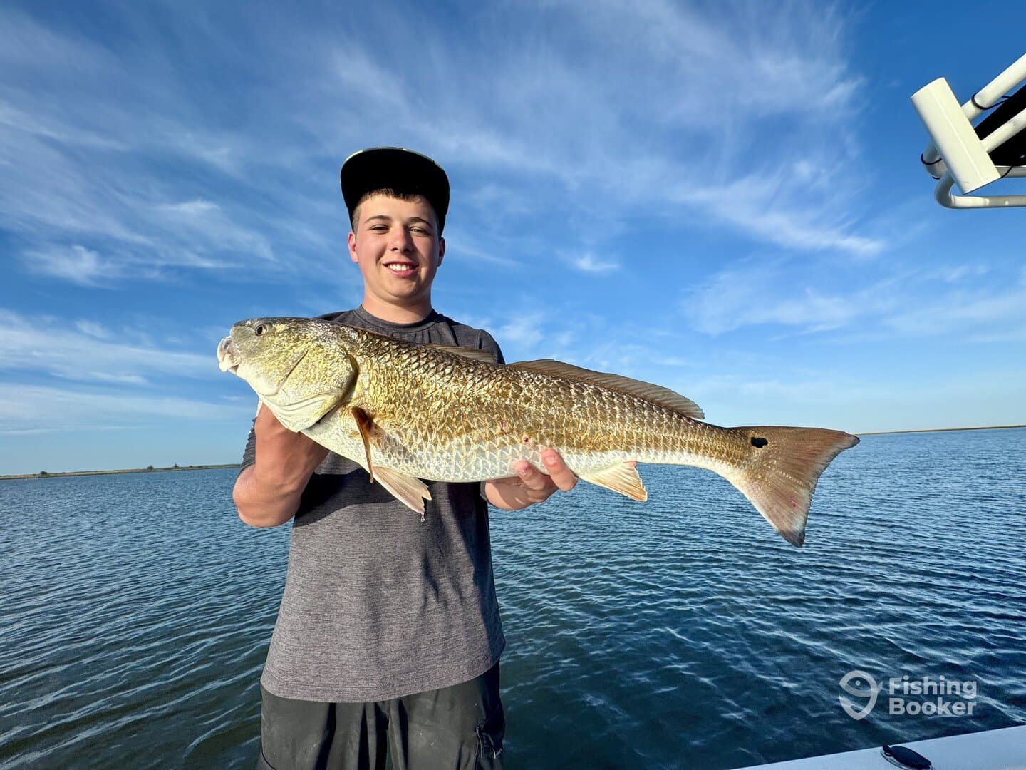 A young angler proudly displaying a large Redfish while fishing in calm waters.