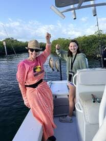 Two anglers, a woman and a young girl, proudly displaying their catch of Snapper while fishing on a boat in a scenic waterway.