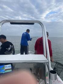 Anglers actively fishing from a boat, with one person reeling in a catch while others assist, showcasing a lively fishing environment.