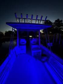 Interior view of a fishing boat illuminated with blue lighting, showcasing seating and console features during twilight.