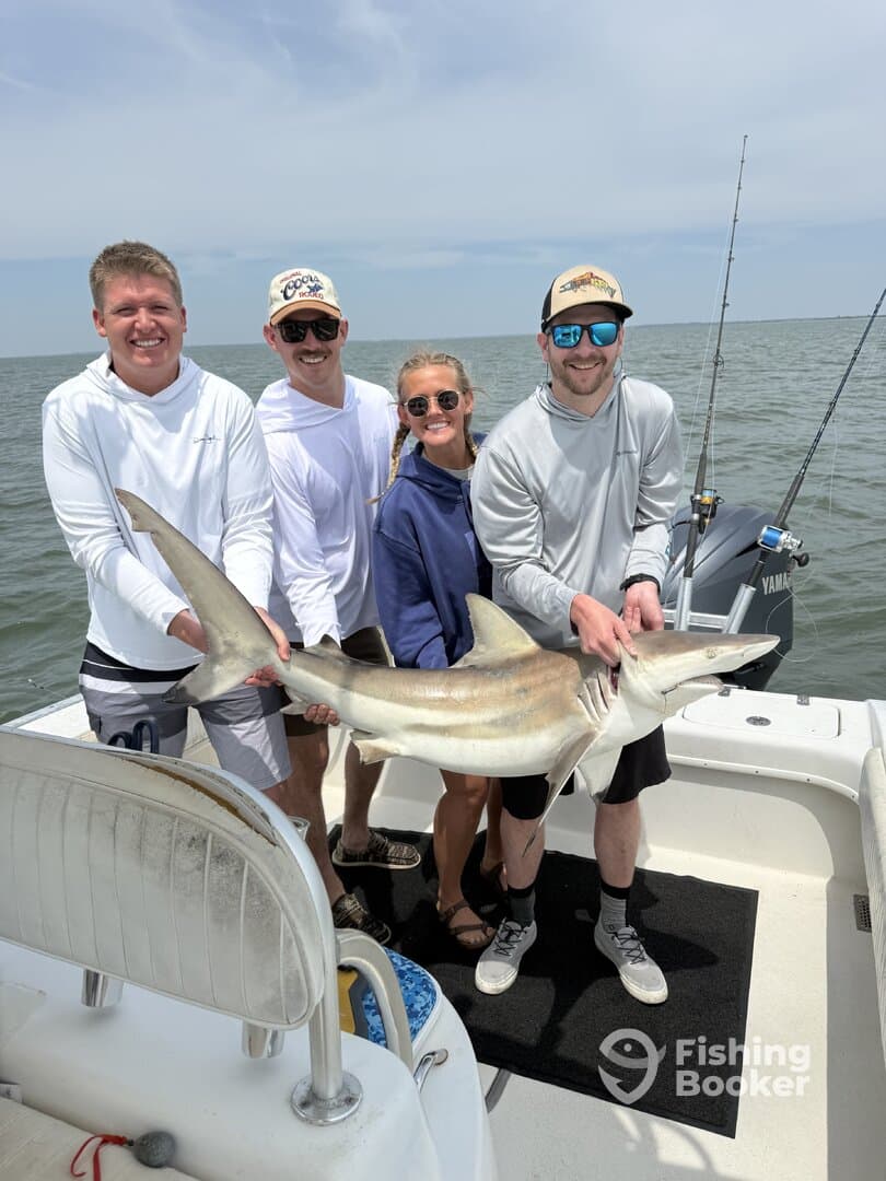 A group of four anglers proudly displaying a large shark while fishing on a boat in open waters.
