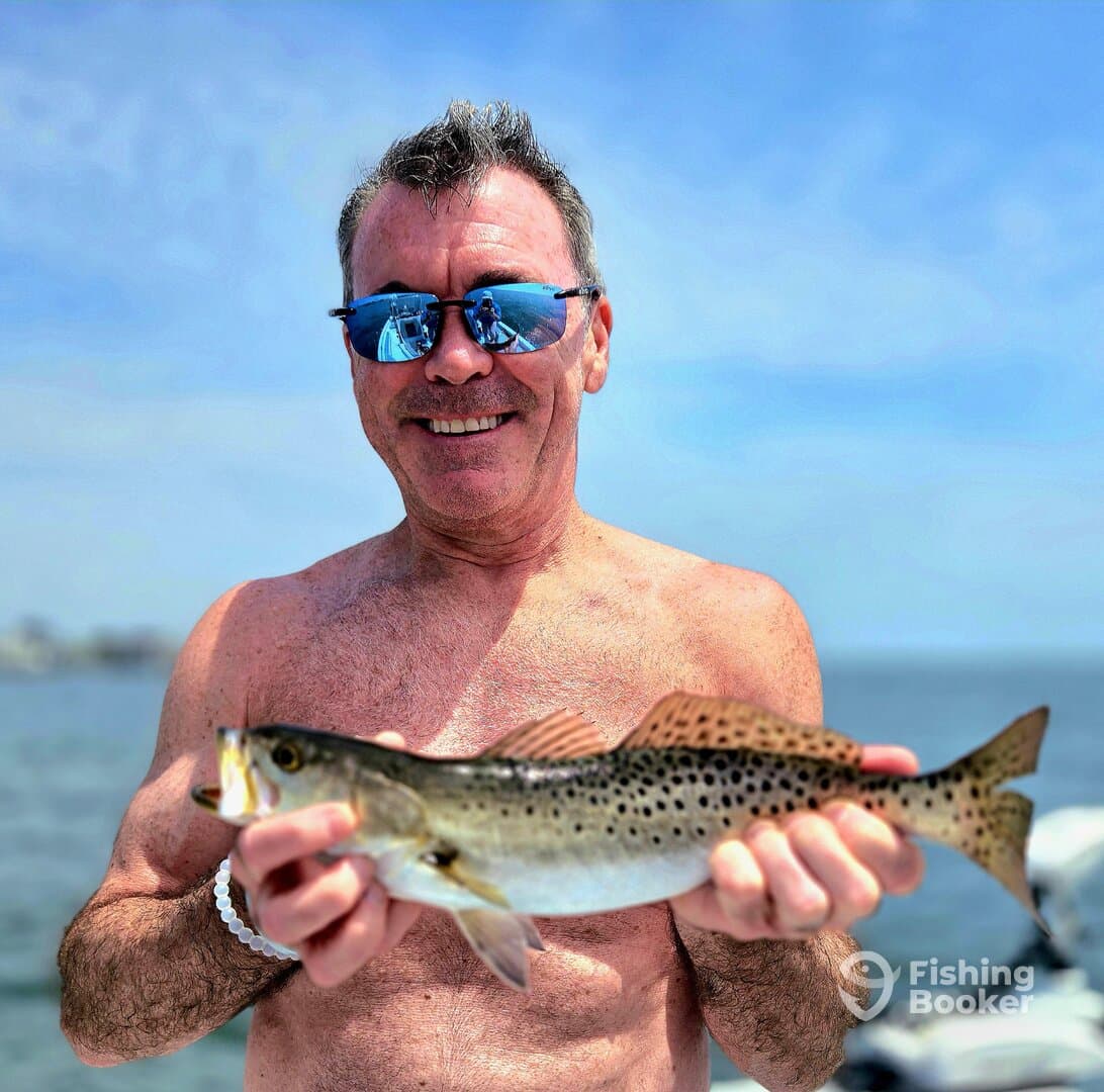 A proud angler displaying a beautiful Speckled Trout while enjoying a sunny day on the water.