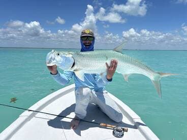 Angler proudly displaying a large Tarpon while fishing in clear turquoise waters.